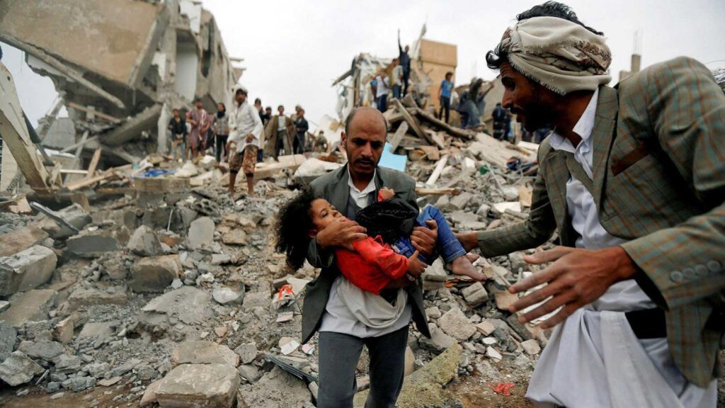 Un hombre lleva a una niña rescatada entre los escombros del edificio derruido tras un ataque aéreo en la capital de Yemen. Foto: Khaled Abdullah.